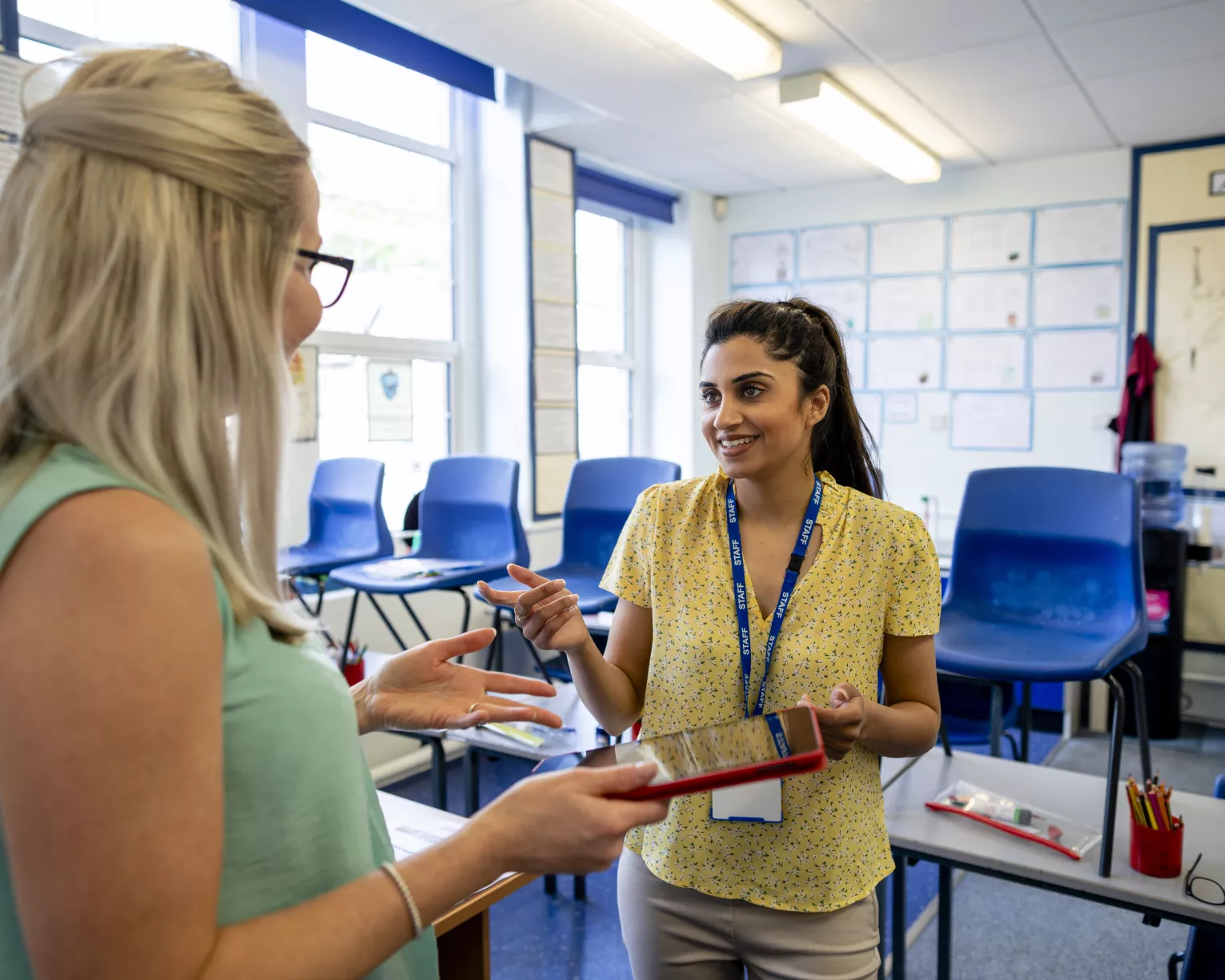 photo of blonde-haired educator speaking to a brown-haired educator in a classroom