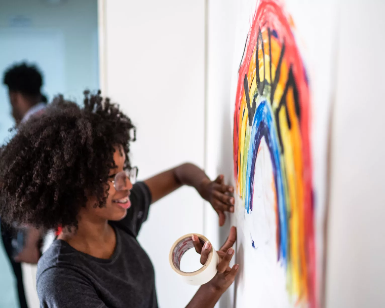 a black girl hangs a poster with a rainbow that says love on it