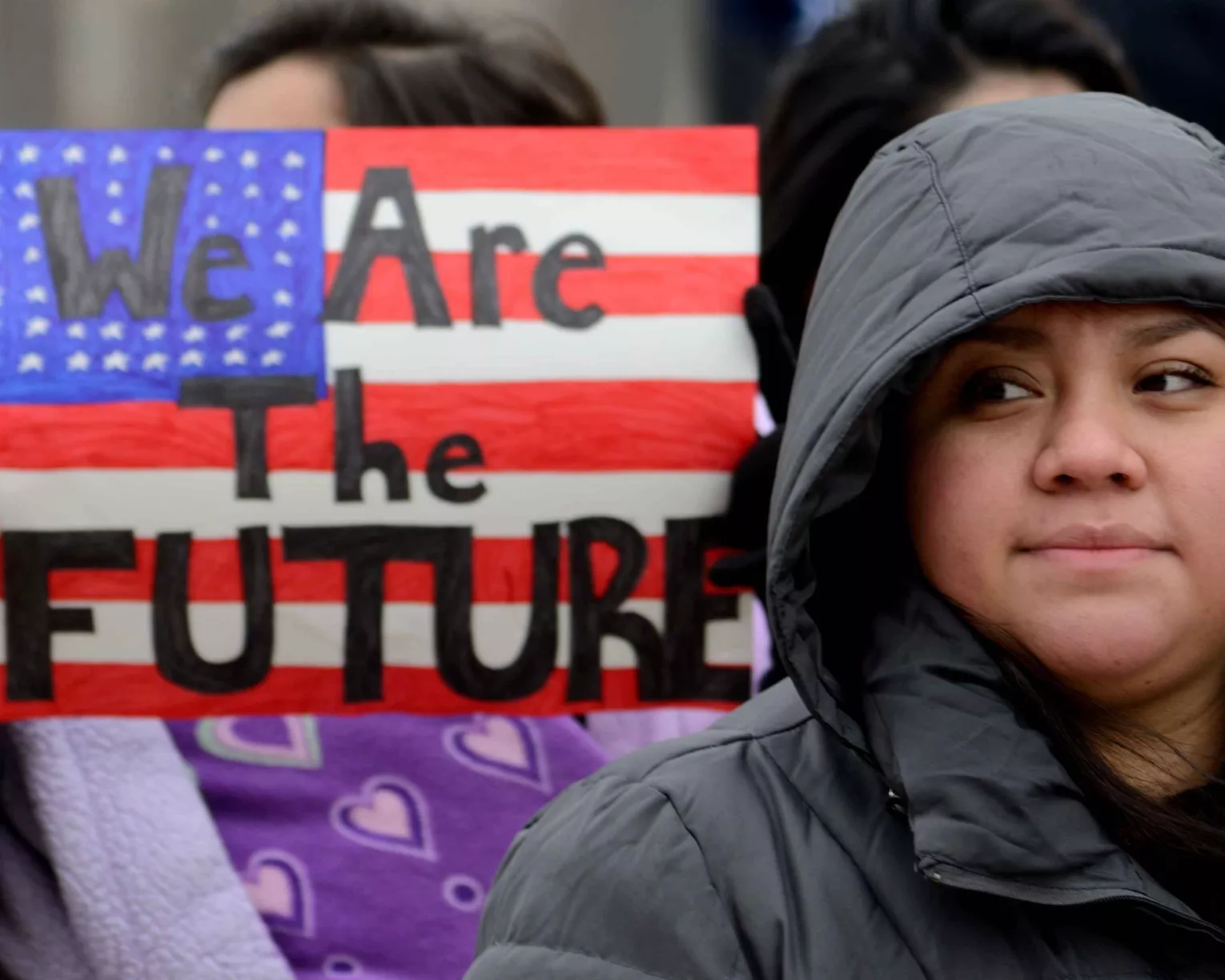Woman outside holding a sign that says "we are the future" in front of an American flag
