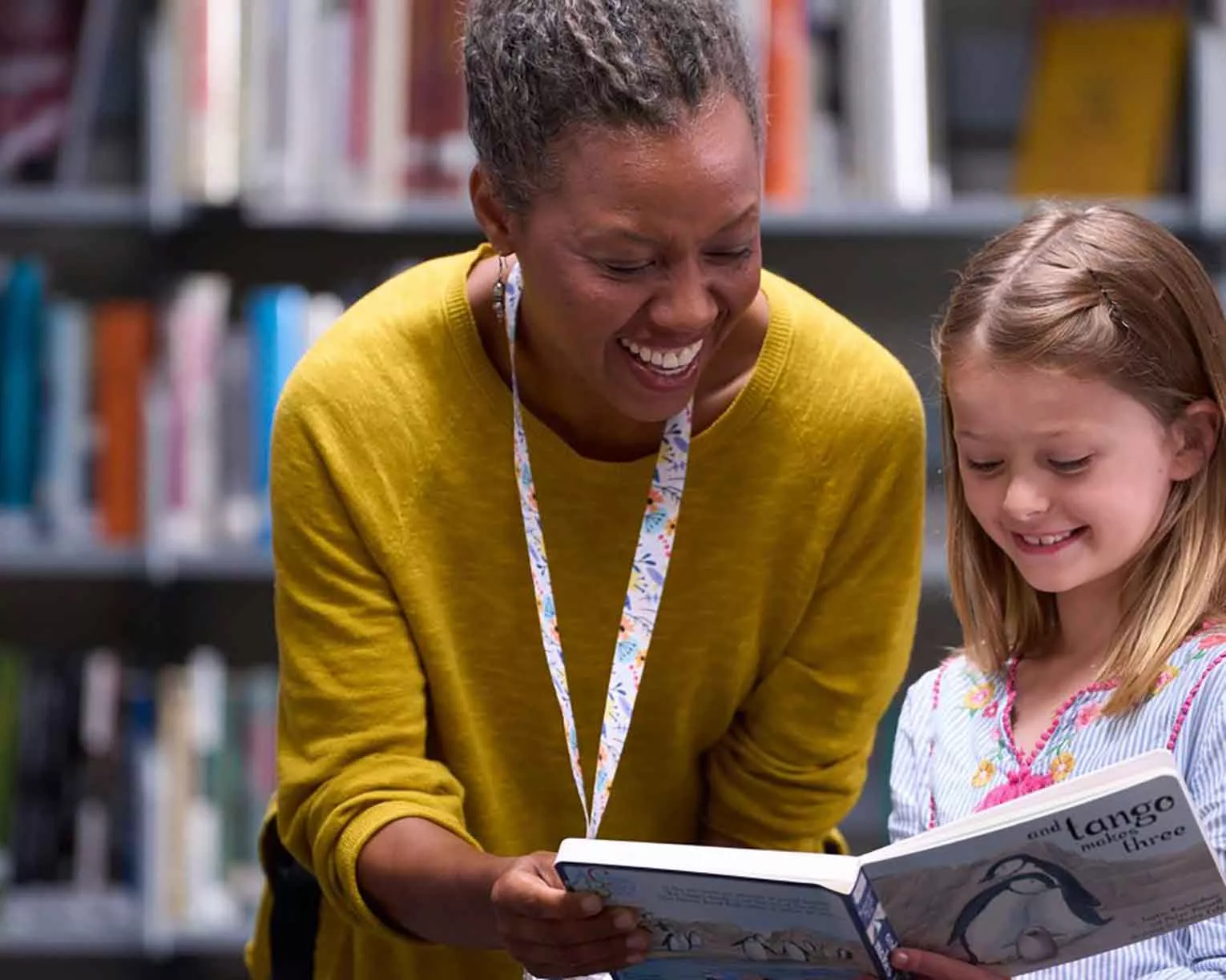 A black female librarian shows a white female child a book in a library setting