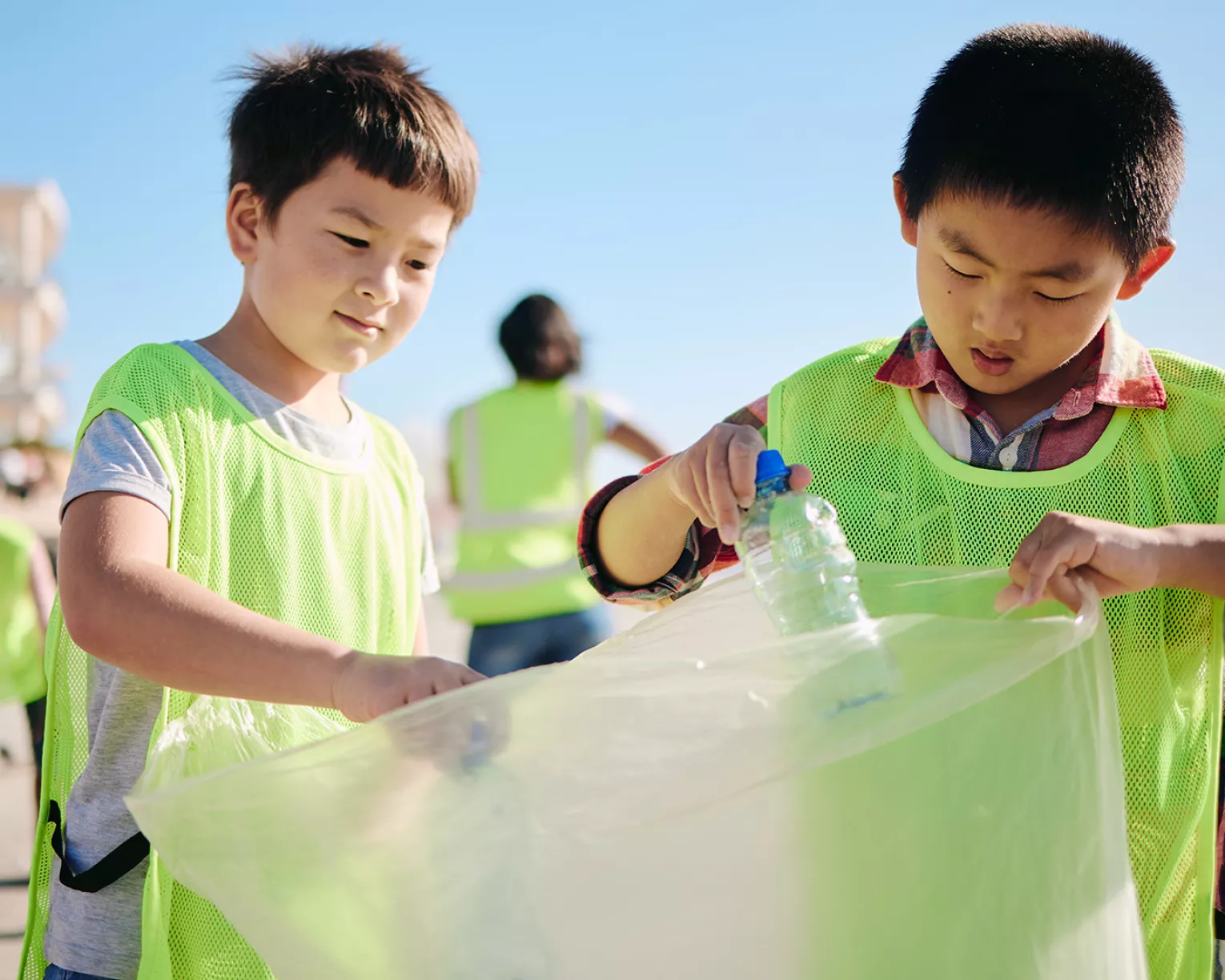 two young boys pick up trash on a sunny beach