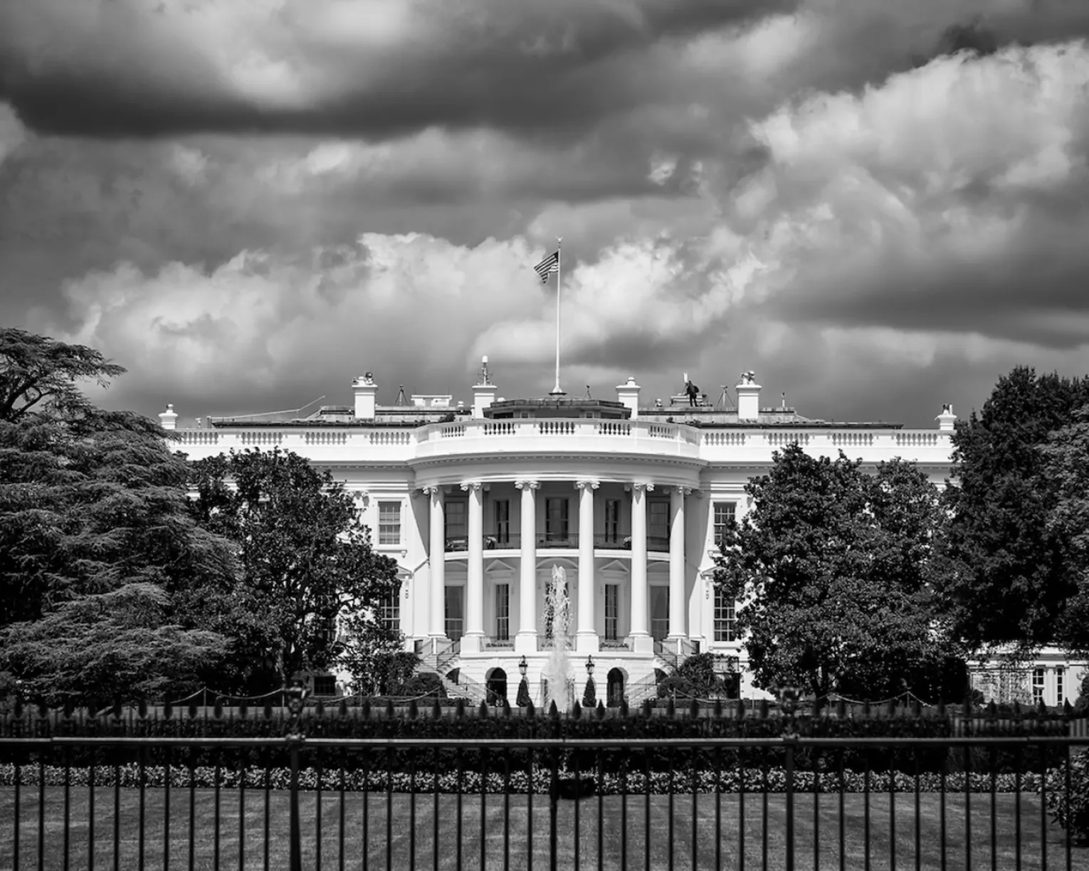 Black and white photo of the White House with storm clouds above