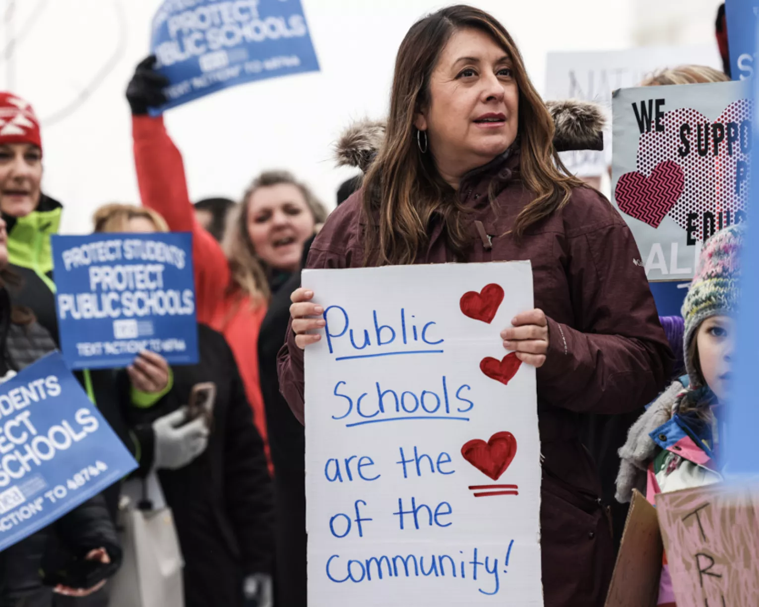 A crowd of people holding various signs about supporting public education.