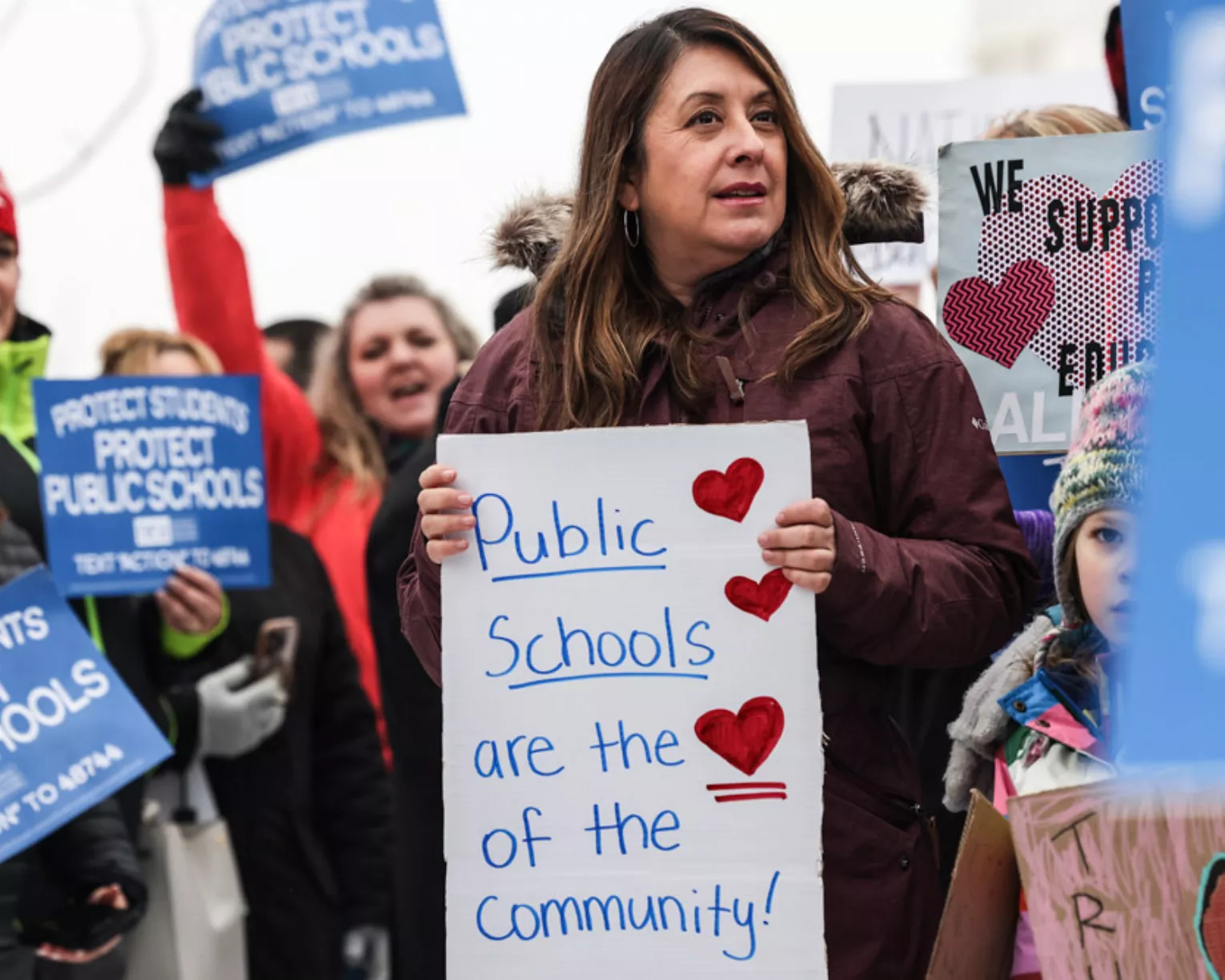 A participant in the crowd at the 2024 Protect Public Schools rally holds a sign that reads  "Public schools are the heart of the community."