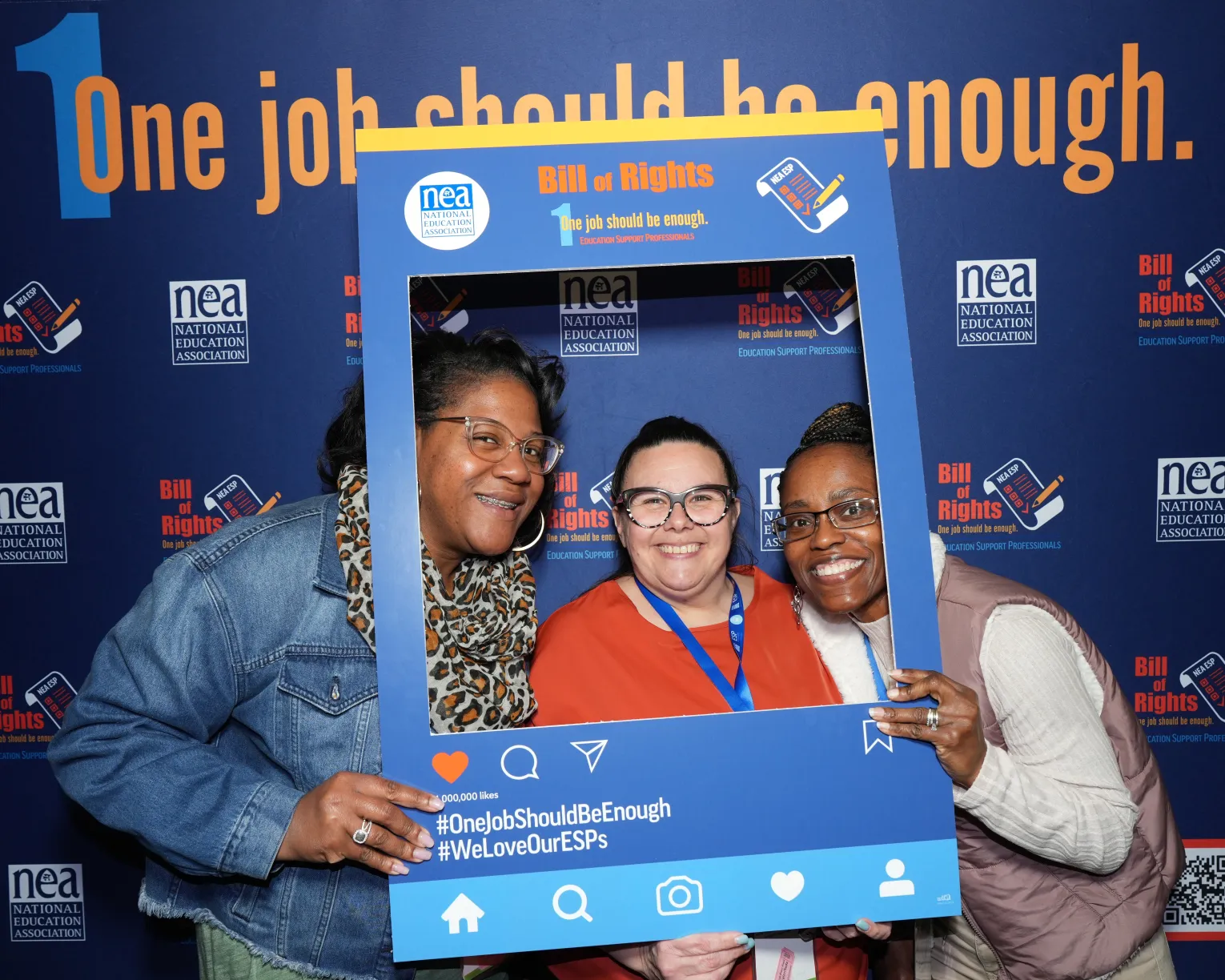 Three women of color standing in front of a backdrop that says, "One Job Should Be Enough," and holding up a dark blue social media frame labeled "NEA ESP Bill of Rights" in orange letters