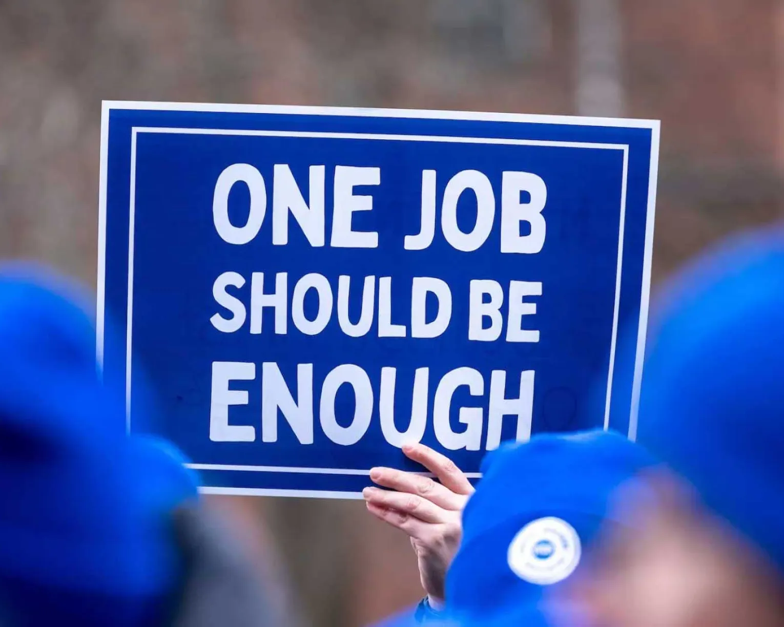 Blue protest sign saying One Job Should Be Enough