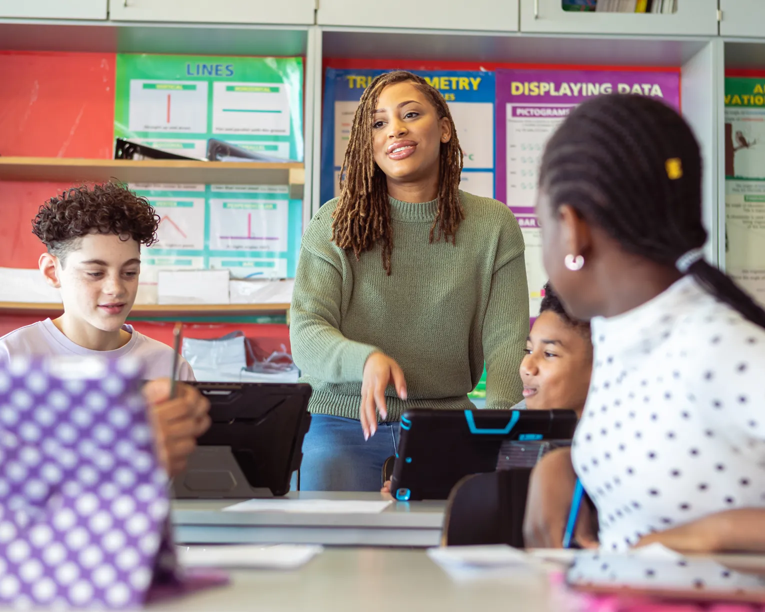 Black female teacher stands next to a table of students in the classroom during a discussion