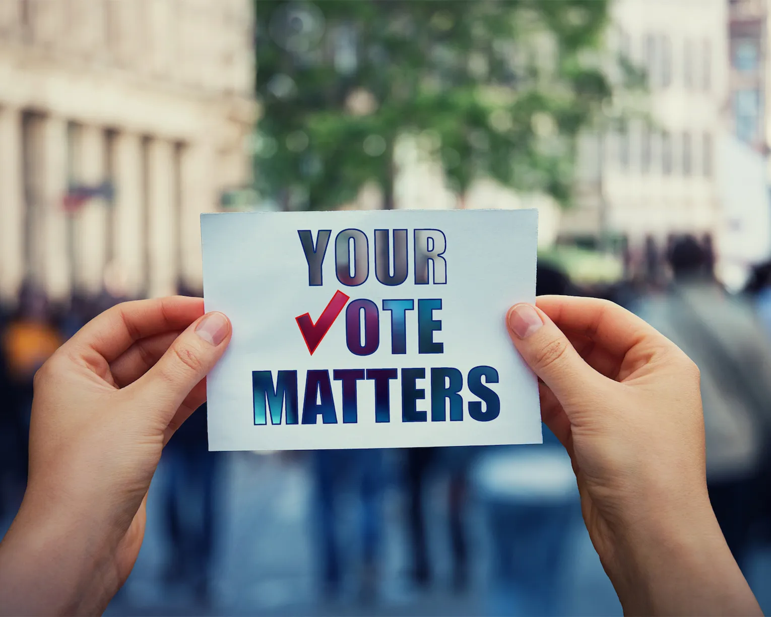 two hands hold a sign that says Your Vote Matters. The V in Vote is a check mark instead of a letter