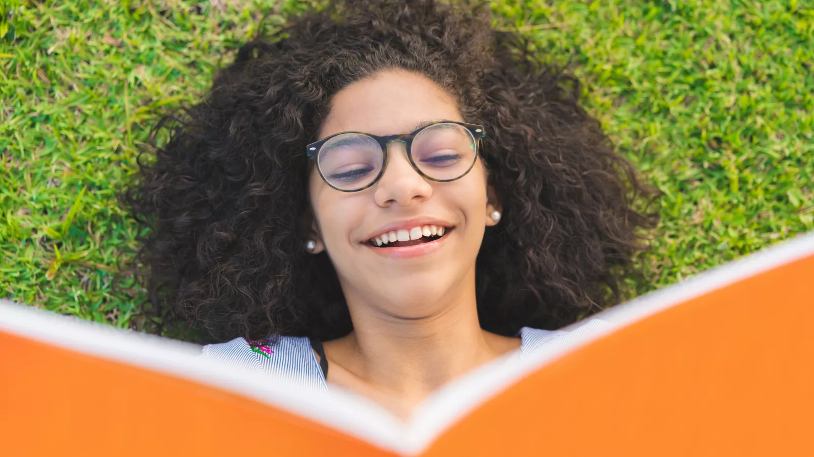 A girl reads a book while lying in the grass