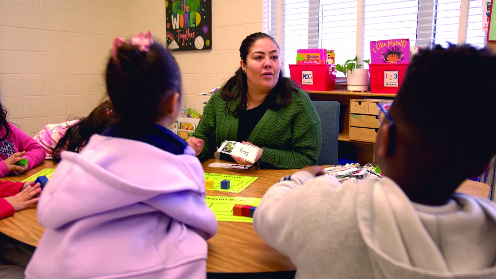 preschool teacher Rita Bamba sits at a table with students using pictures and blocks to teach