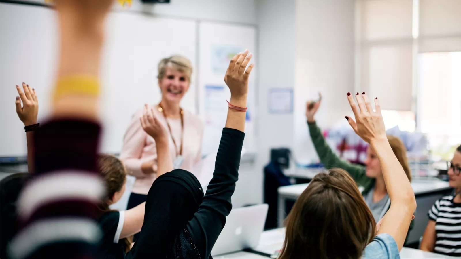 Teacher stands in front of classroom and calls on students with raised hands