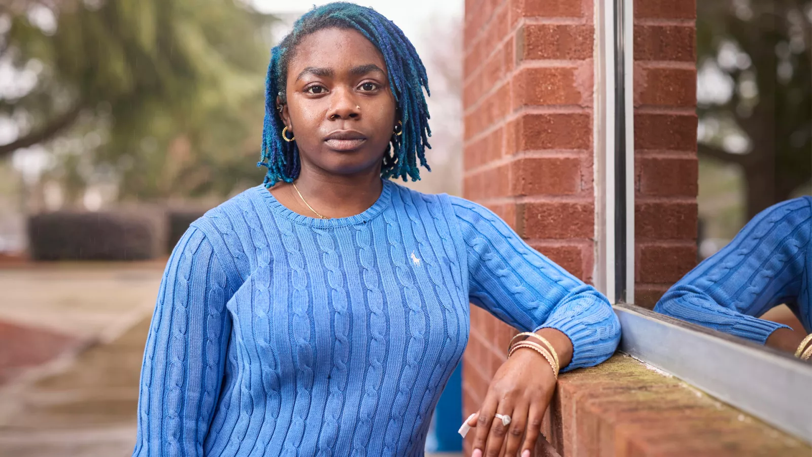 A woman in a blue sweater looks directly into camera with a determined look.