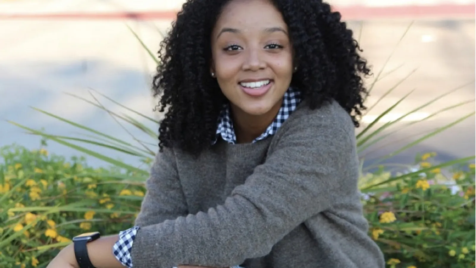 A woman sitting outside with her leg crossed over the other smiles directly to camera.