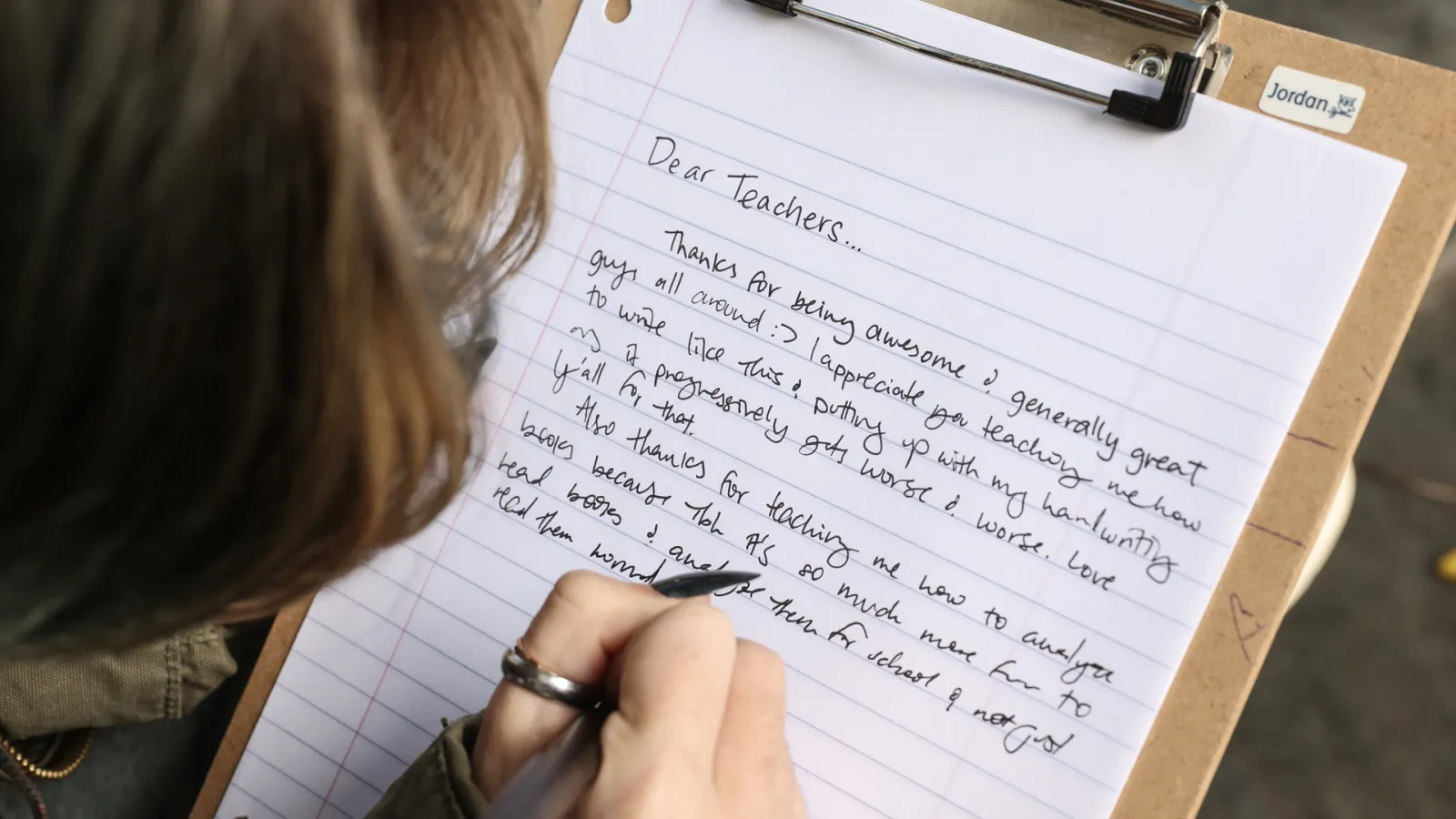 A person writes on lined school a paper a Dear Teacher letter.