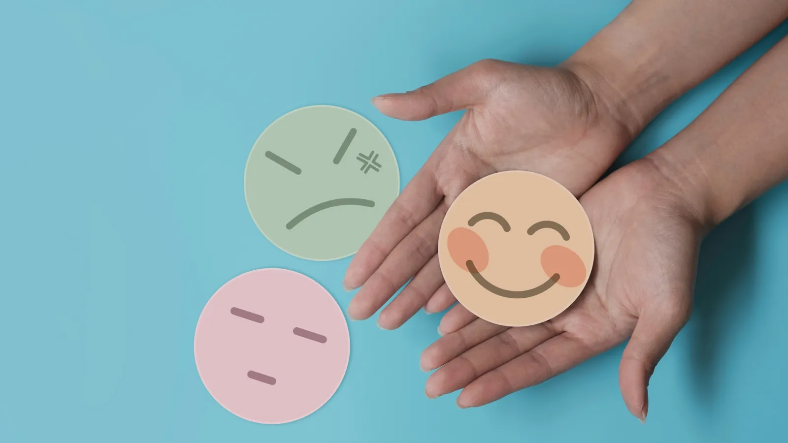 Hands holding a smiling emoji, with two other emojis, one angry and one indifferent, placed on a blue background,