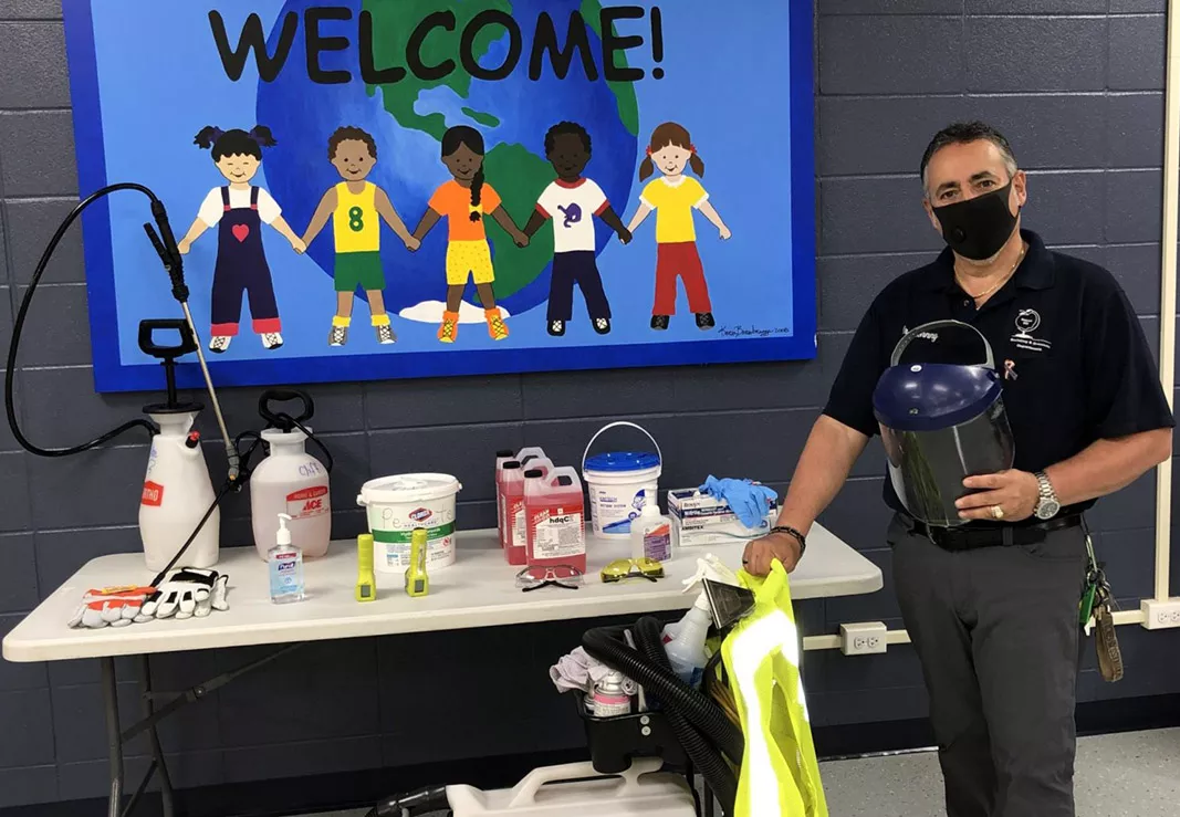 A school custodian wearing a mask cleans a classroom