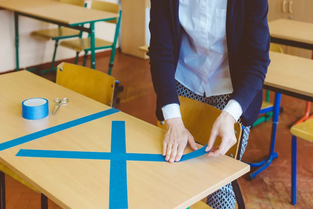 A teacher marks a desk with masking tape