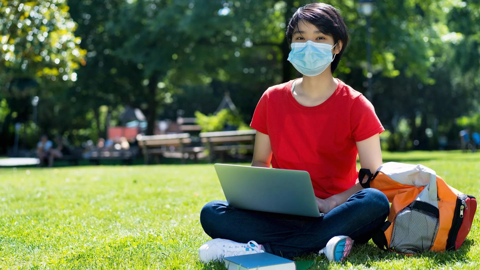 A young Asian woman sitting in the grass with a laptop
