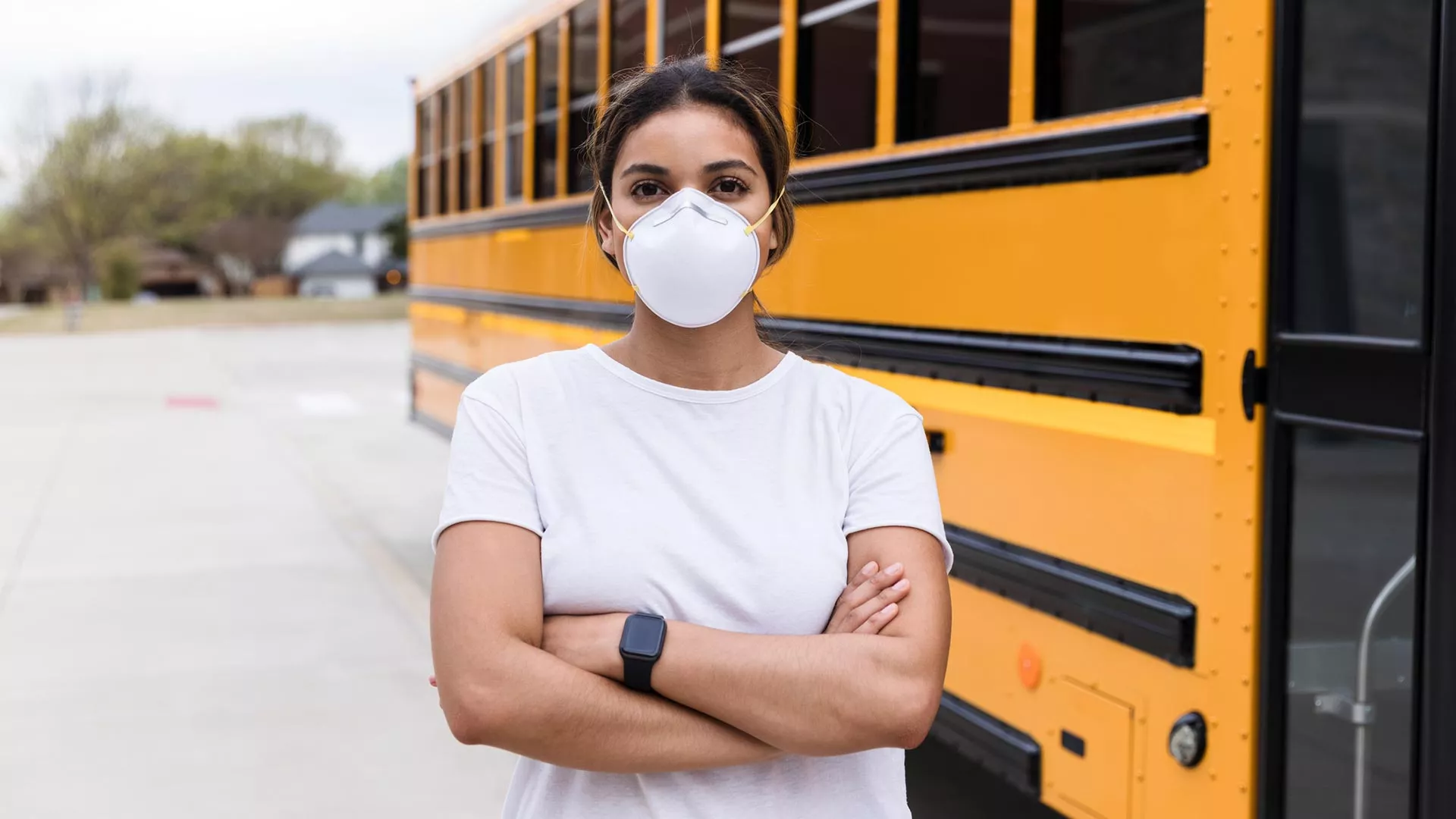 A bus driver with folded arms wears an N95 mask