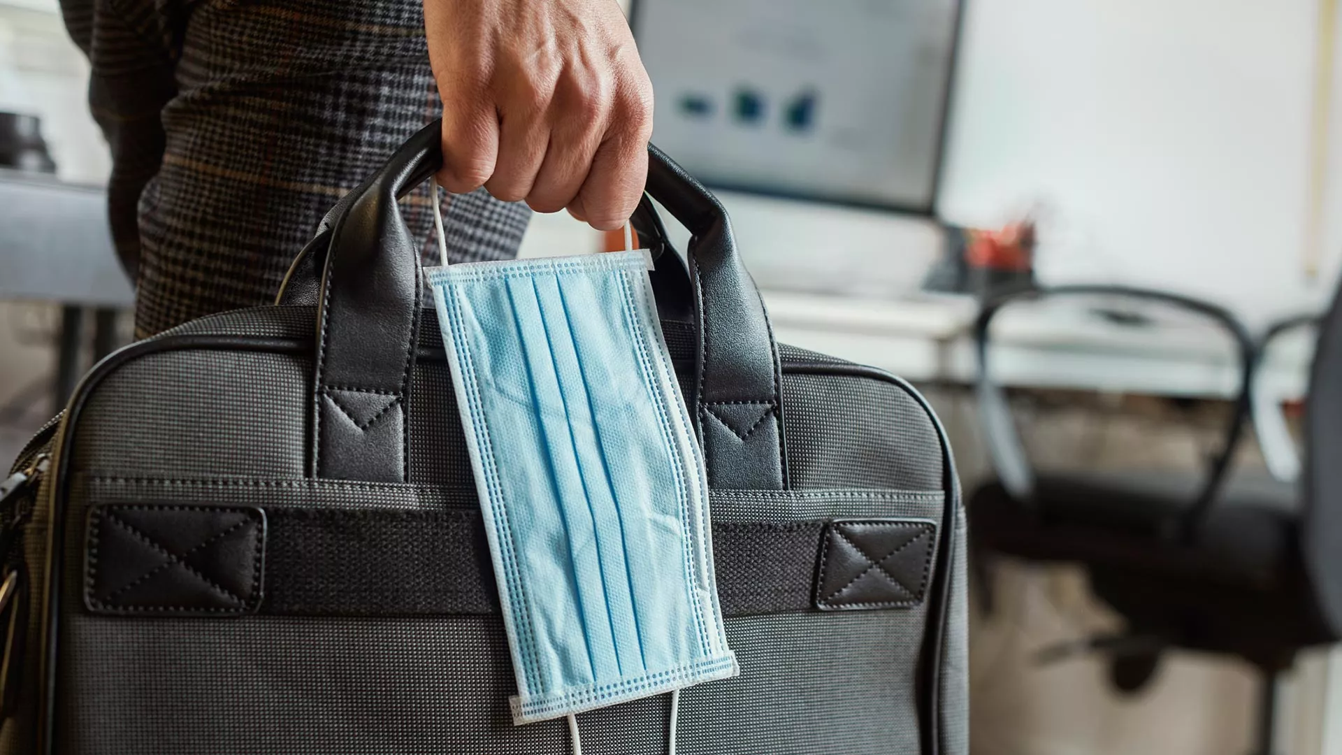 A man carries a mask and briefcase into workplace