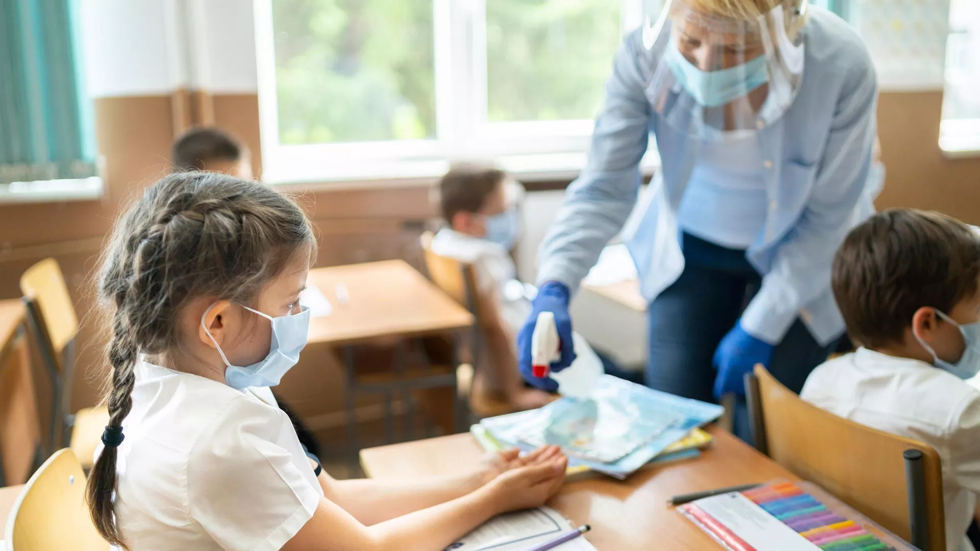 A teacher sprays a young girl's hands with sanitizer in a classroom