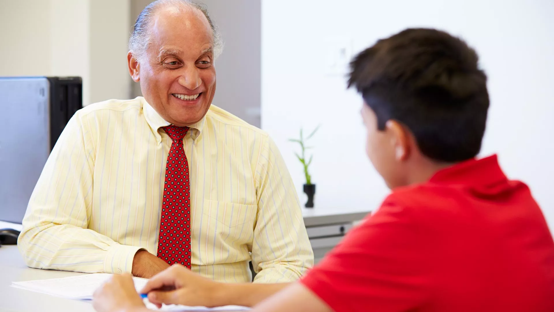 A male school counselor chats with a young male student