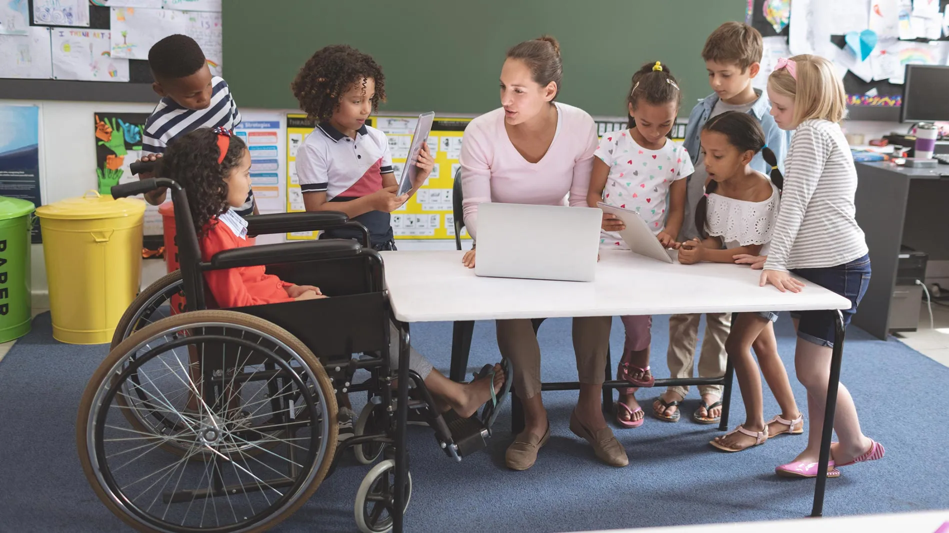 A teacher speaks to students, including a young girl in a wheelchair