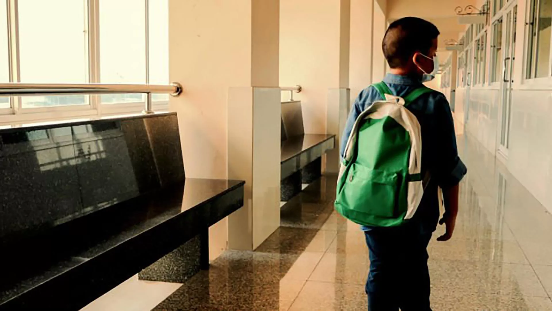 A young boy walks down an empty school hallway
