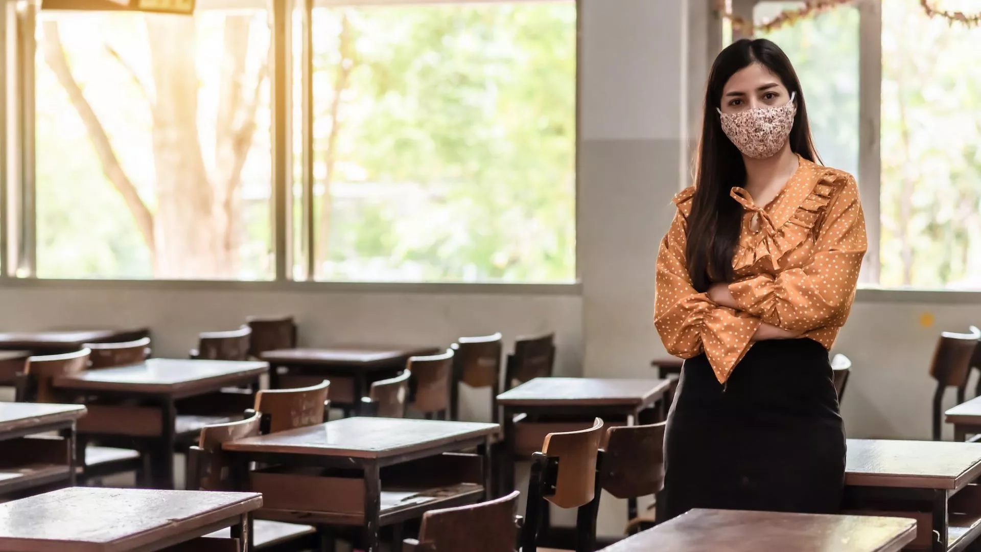 A teacher wears a mask in an empty classroom