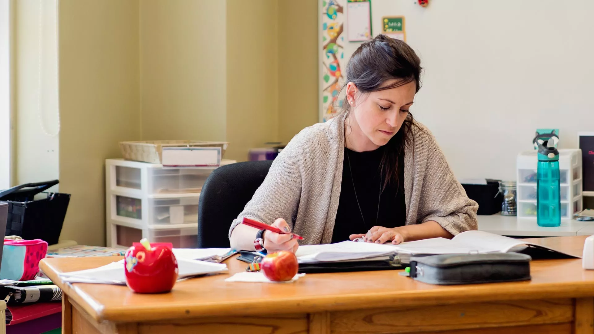 A teacher looks over papers at her desk in an empty classroom