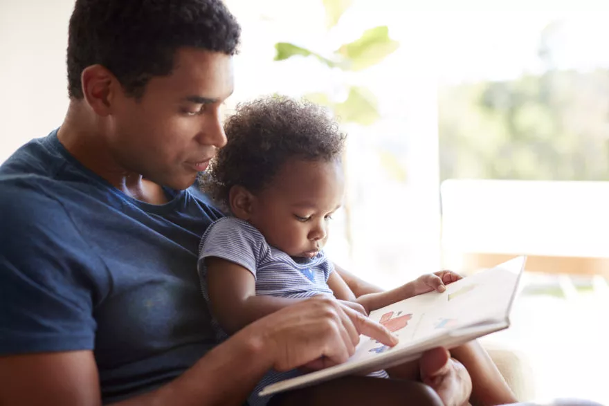 A man reads to a toddler sitting in his lap
