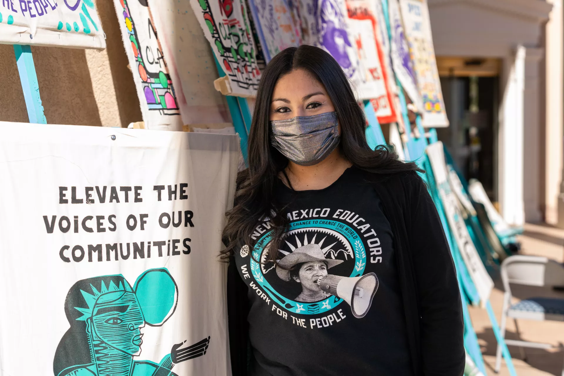 New Mexico educator stands in front of signs asking for respect for educator voices.