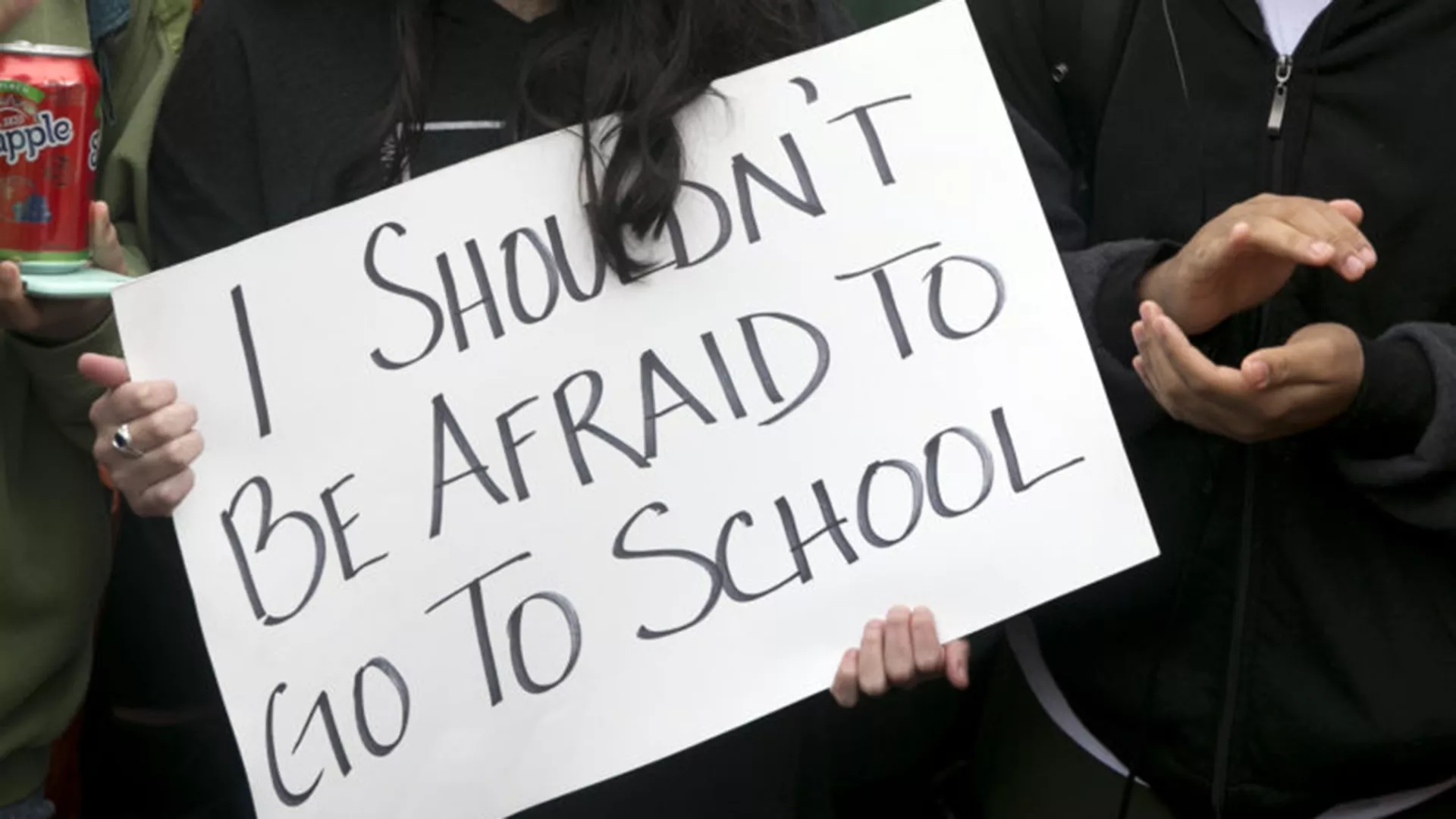 person holding protest sign that says I shouldn't be afraid to go to school