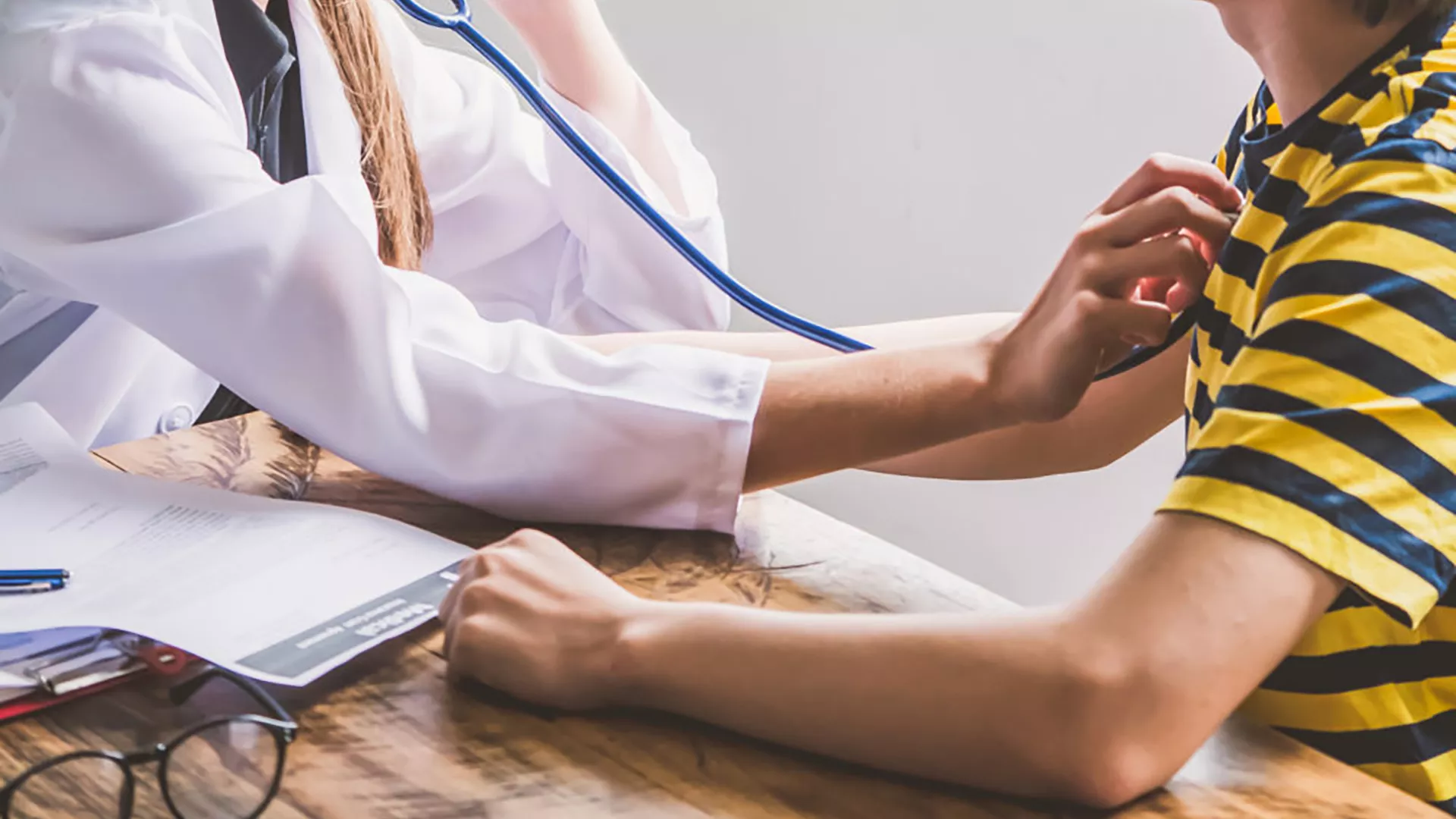 Doctor holds up stethoscope to child in striped shirt.