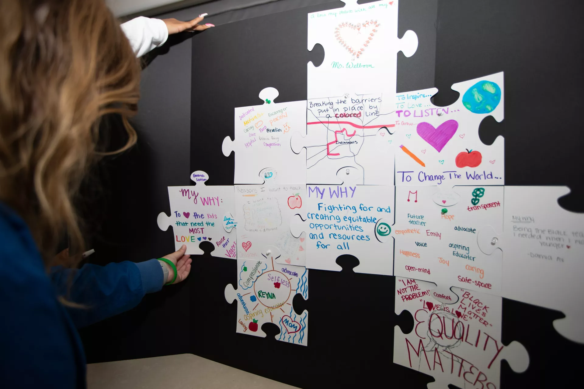 Photos of oversized puzzle pieces with messages of why future teachers choose to teach. 