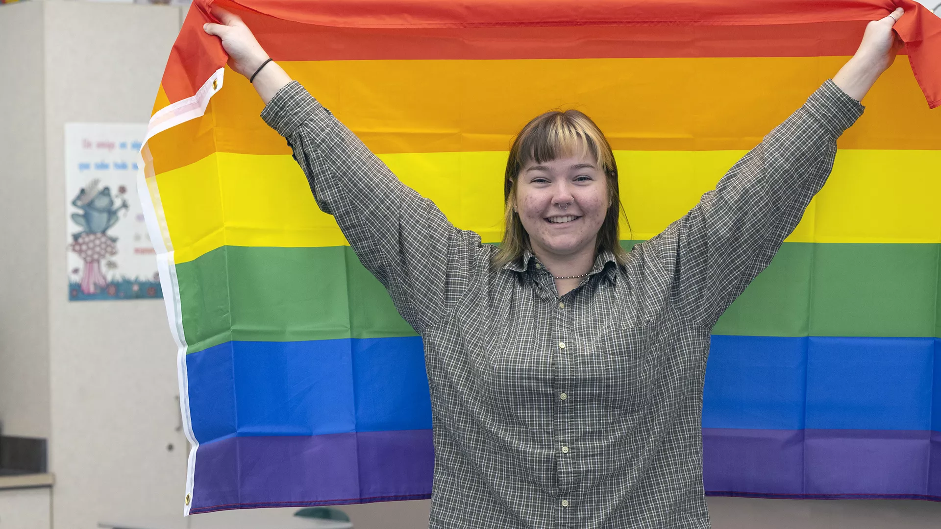Student holds up rainbow flag in school hallway