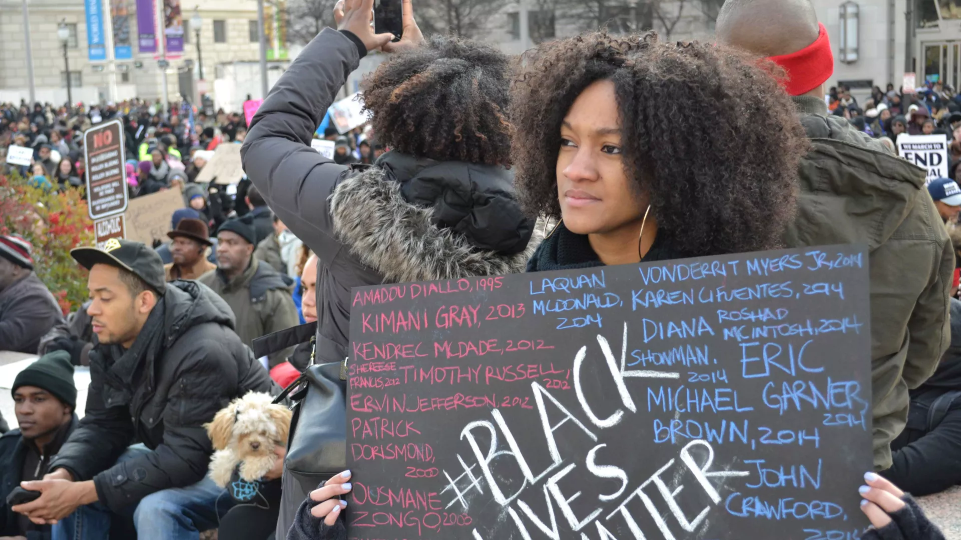 A young Black woman holds a BLM sign at a march