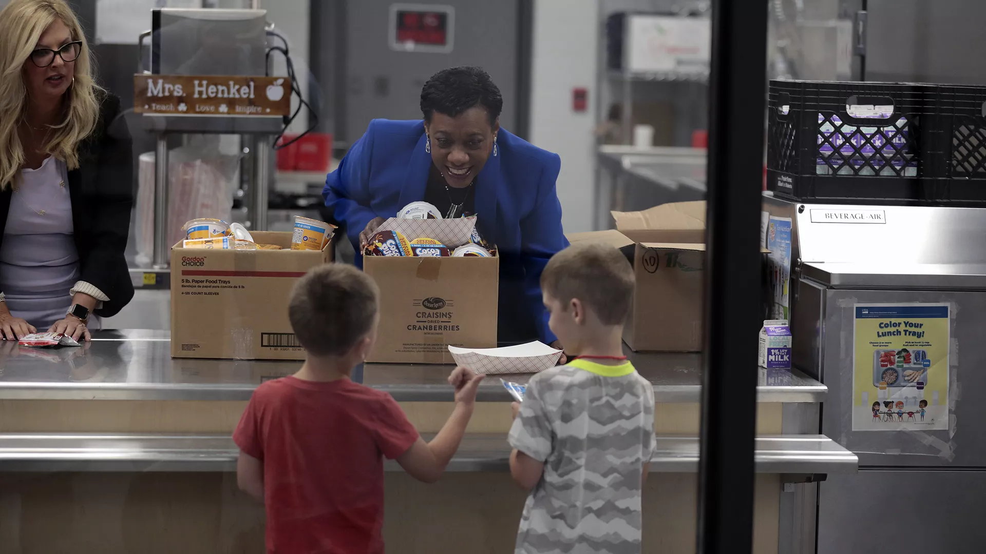 NEA President Becky Pringle hands out food to 2 young students in an elementary school cafeteria