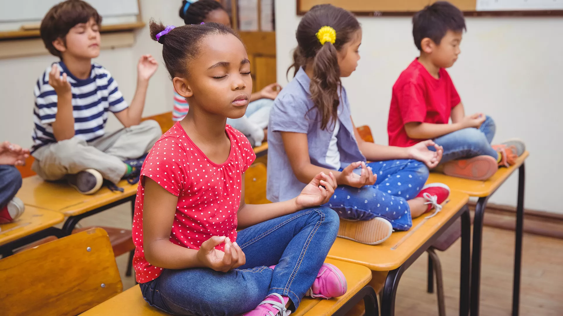 elementary students sit on top of school desks and meditate