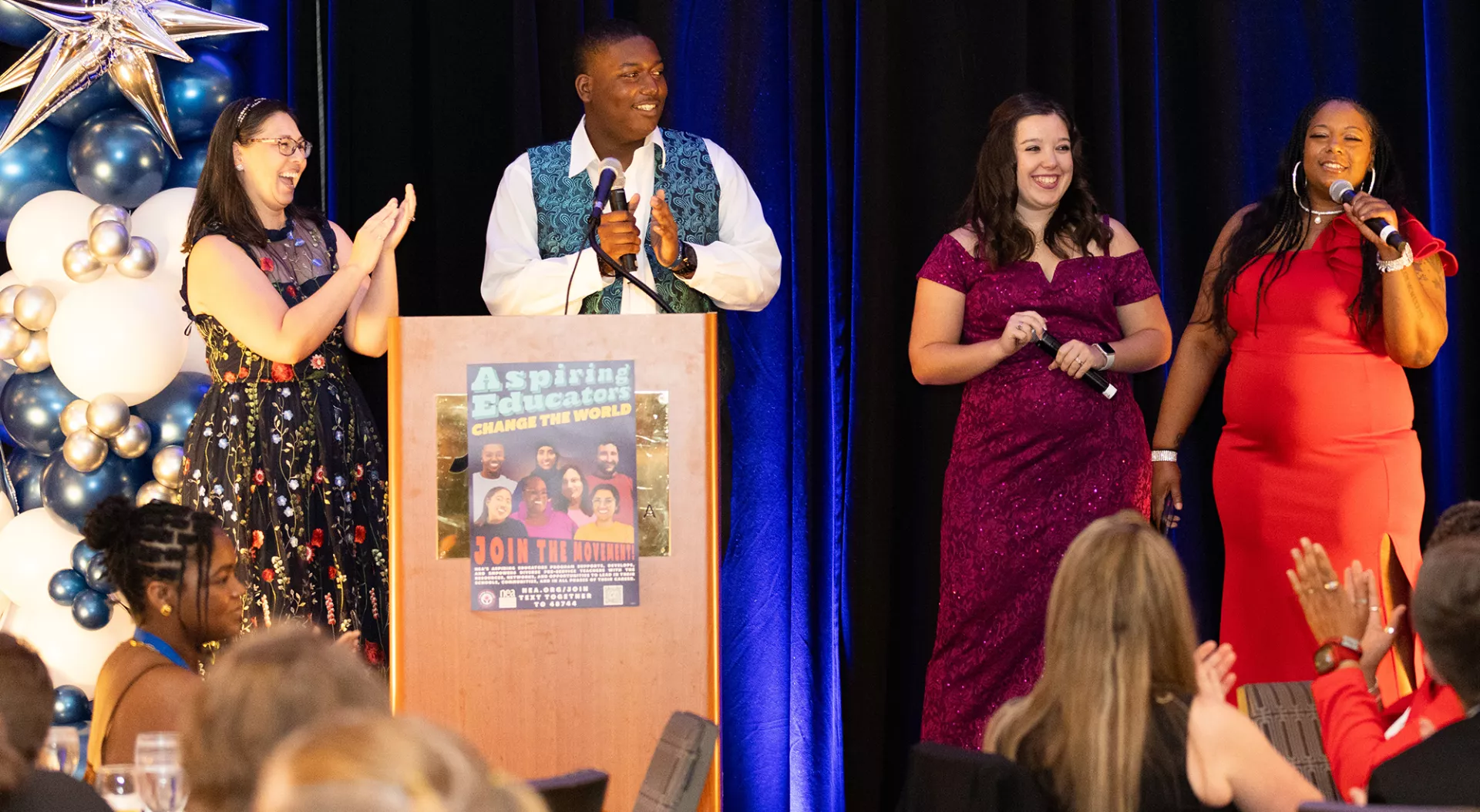 Group of four Aspiring Educators in formal attiring celebrating on stage.