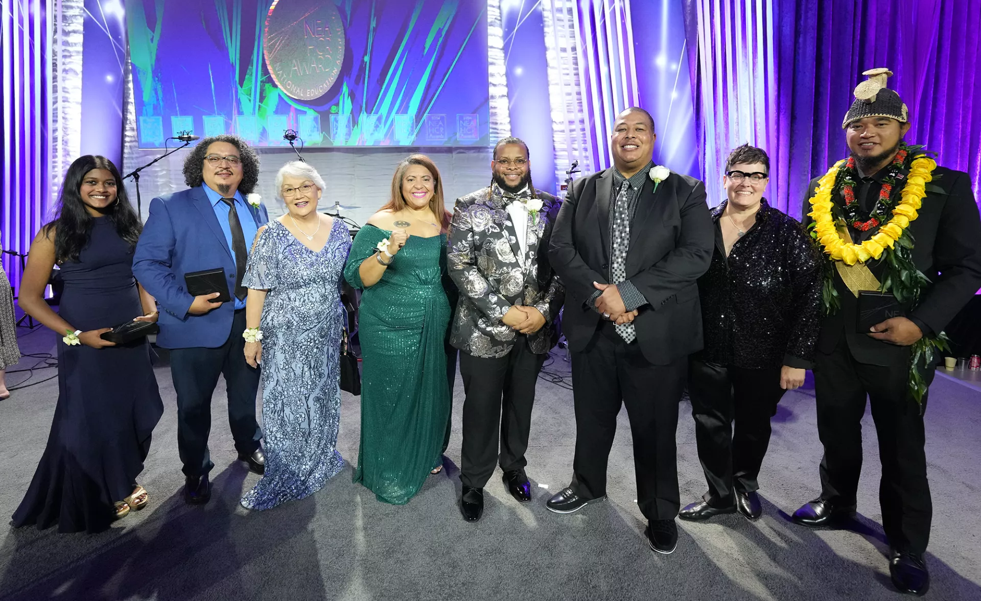 Group of people in formal attire stand near stage during awards ceremony.