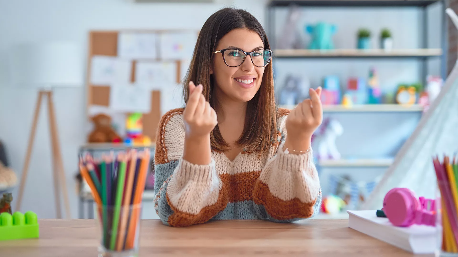 A woman seated behind a desk making a gesture of money with her hands.