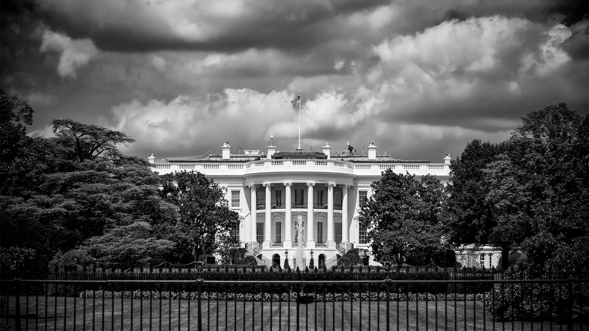 Black and white photo of the White House with storm clouds above