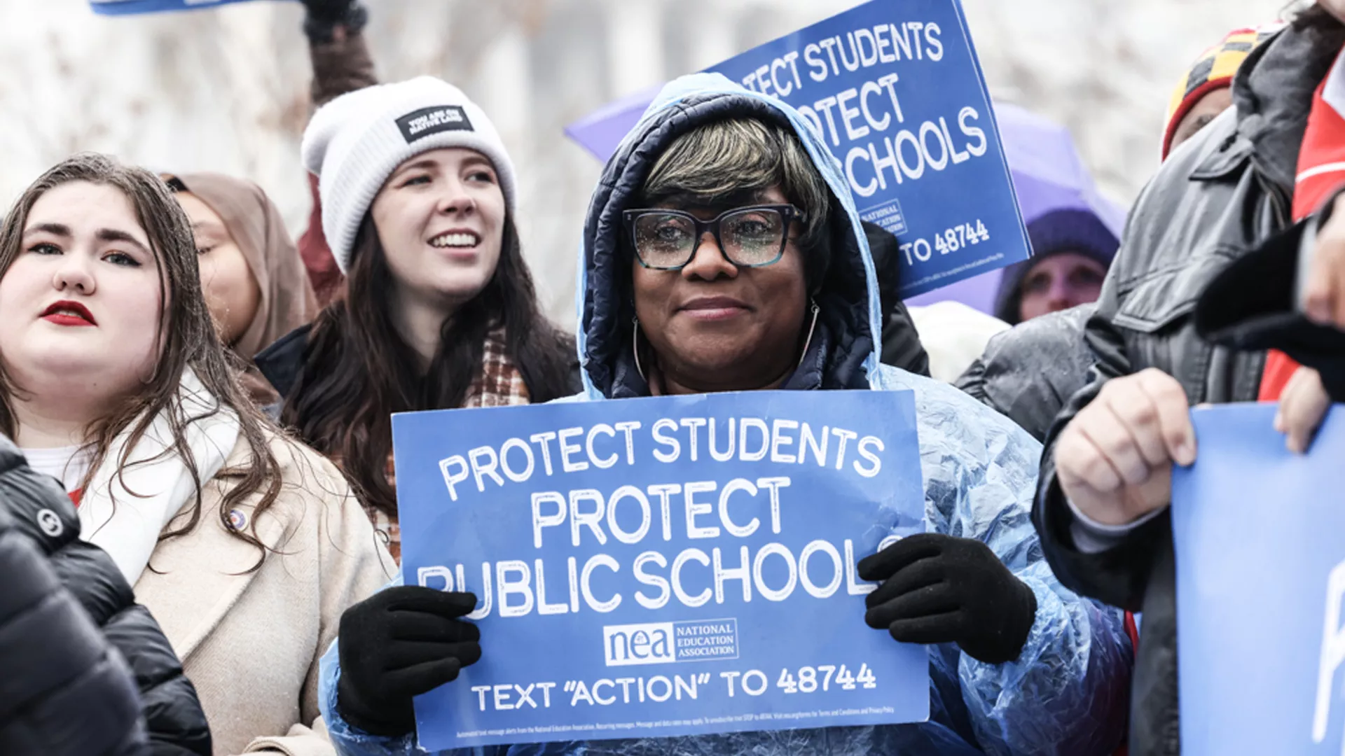 People united in a demonstration, displaying signs that show the importance of safeguarding students and public education.