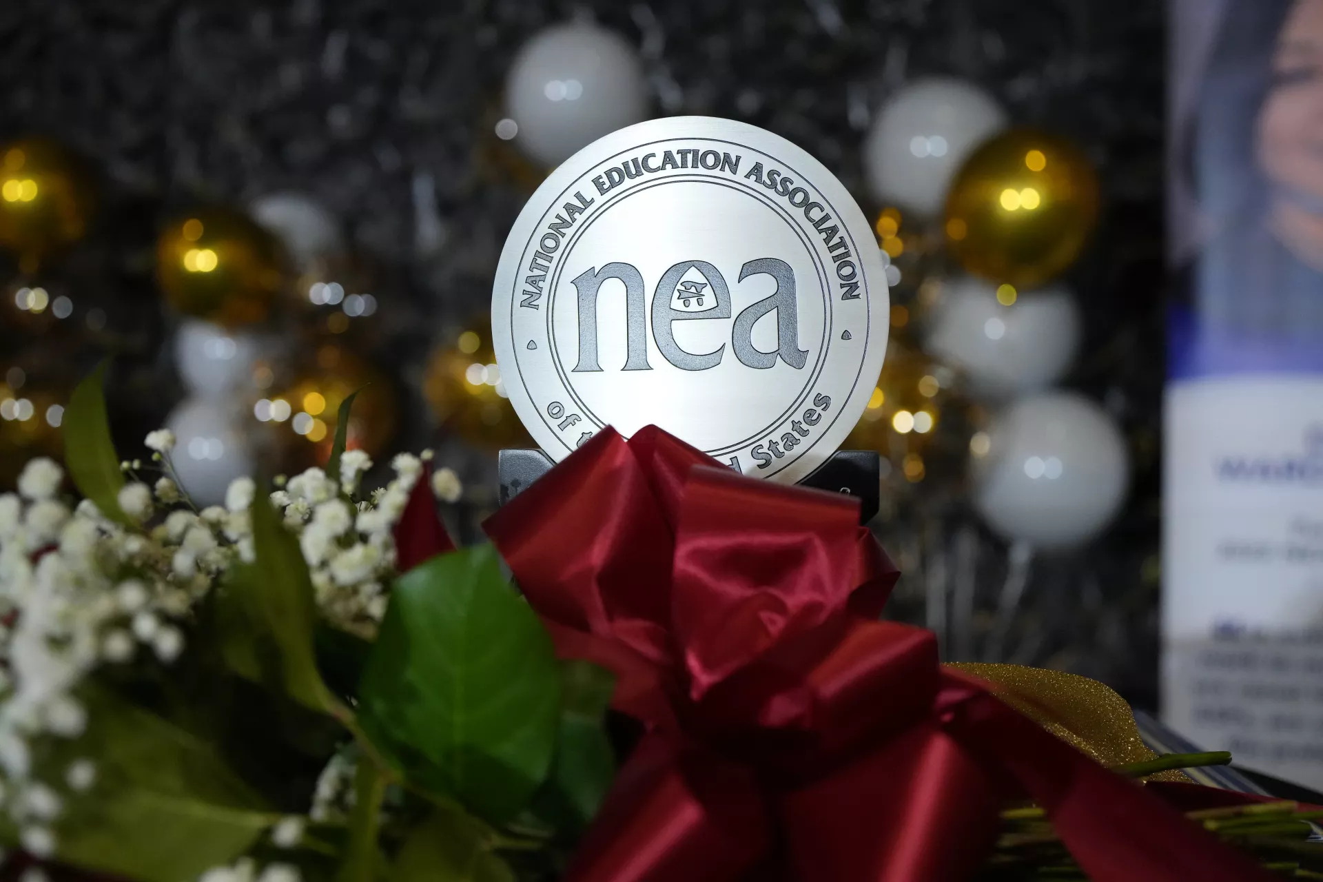 a dozen red roses tied by a red ribbon surrounding a circular trophy with "NEA" printed in the middle of the circle, and "National Education Association of the United States surrounding the "NEA"