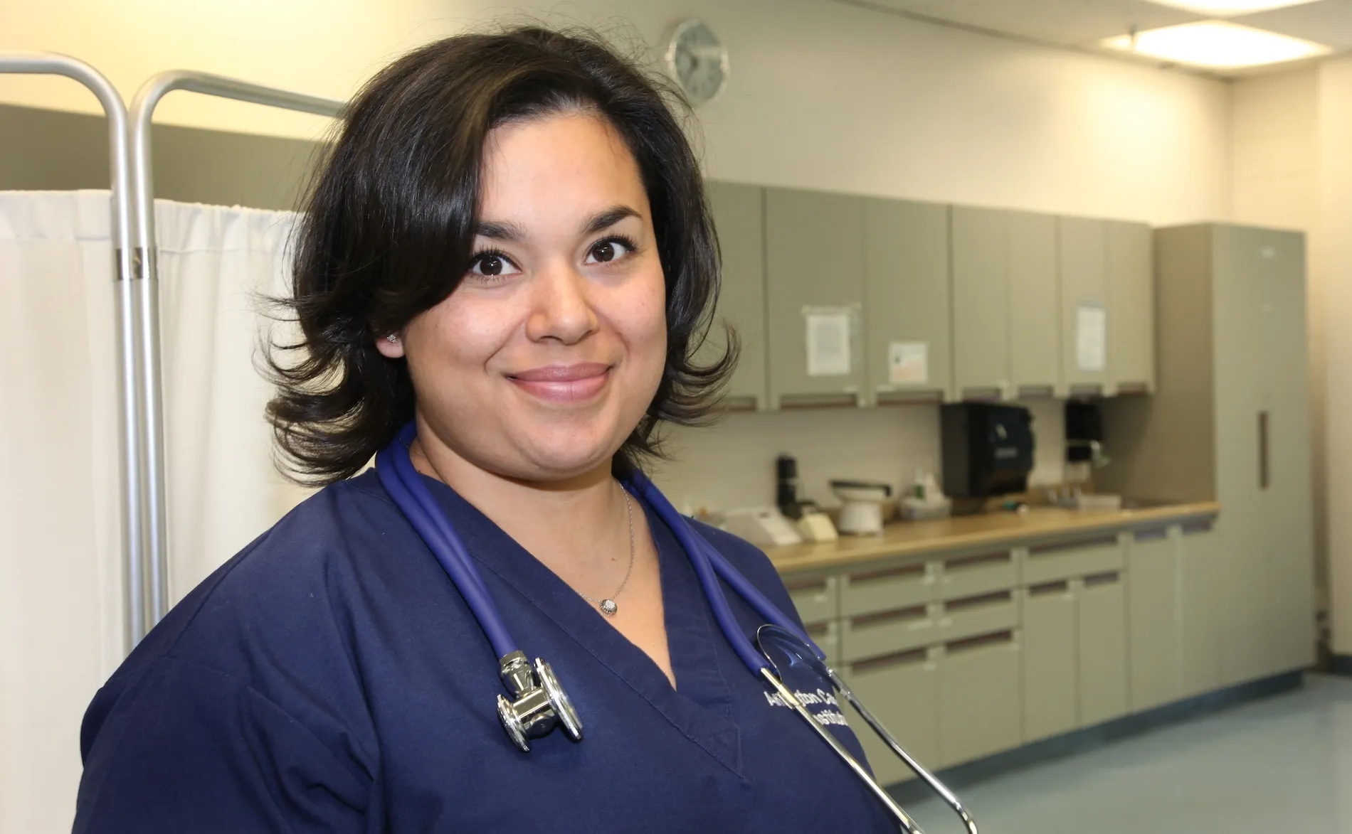 Female school nurse with dark hair in blue scrubs faces camera
