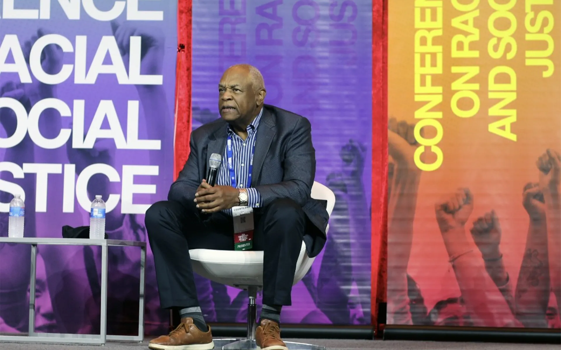 a black man sits on stage with a microphone at the 2025 Conference on Racial and Social Justice