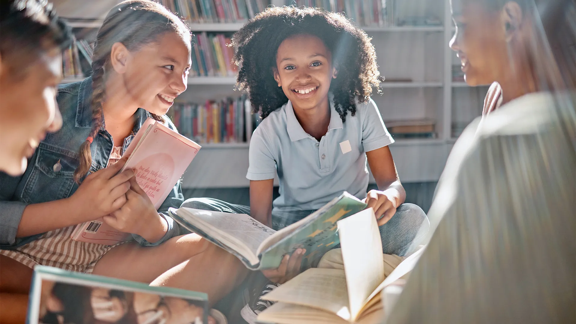 4 students sit and smile in library reading their own books