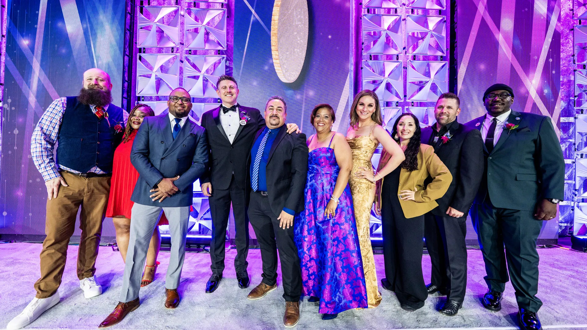 A group of people in formal attire stand on state to pose for a group picture