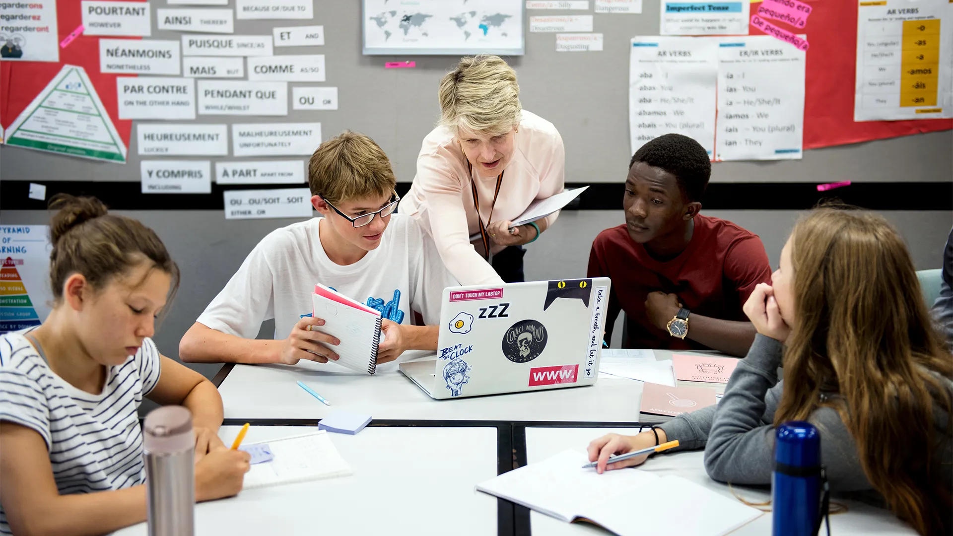 white female teacher works with students at a table on an assignment